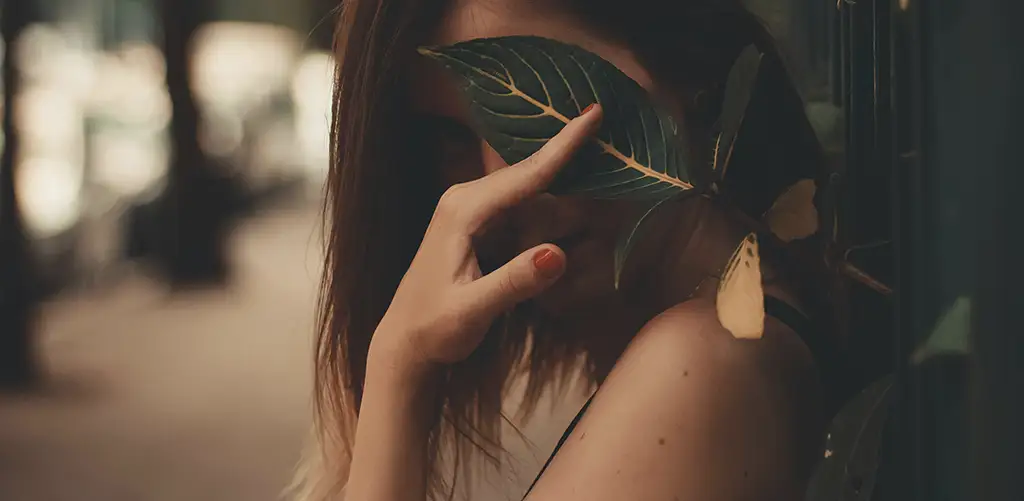 une femme aux cheveux bruns et aux ongles rouges cache son visage avec un congé