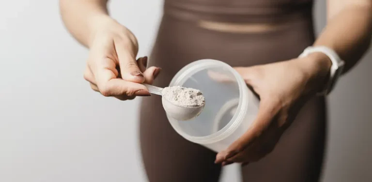 Eine Person hält einen Messlöffel Pulver über einen transparenten Shaker, bereit, ein Nahrungsergänzungsmittel anzurühren.